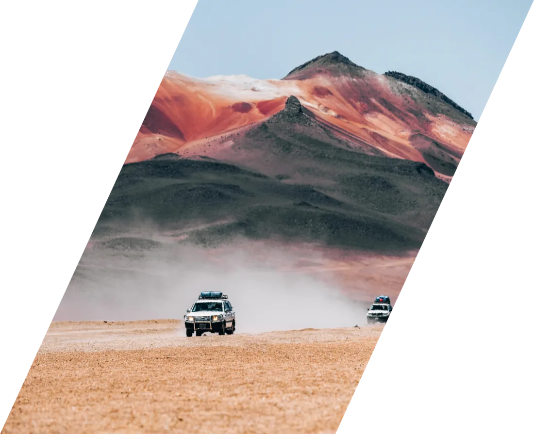 Two four-wheel drives crossing a desert plain below a red mountain range